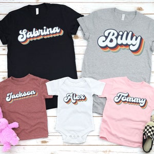 May include: Five t-shirts with retro-style names printed on them. The shirts are in different colours and sizes. The names are "Sabrina", "Billy", "Jackson", "Alex", and "Tommy".