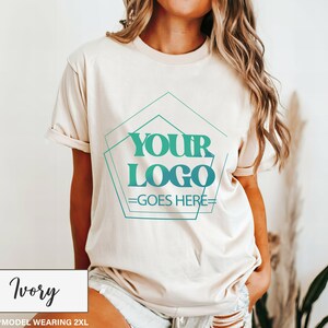 May include: Ivory-colored t-shirt with a crew neck and rolled-up sleeves. The shirt features a teal and green geometric design with the text "YOUR LOGO GOES HERE." The bottom left corner displays the word "Ivory" in a white box.