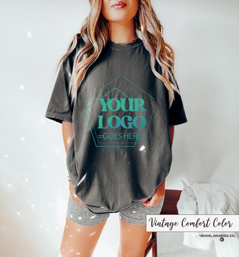 May include: Dark gray t-shirt with the text "YOUR LOGO GOES HERE" in a teal and turquoise design. The shirt is a vintage comfort color and is a 2XL size.