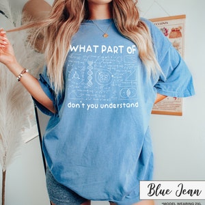May include: Blue jean colored t-shirt with the text "WHAT PART OF don't you understand" in white. The shirt features a graphic of scientific formulas and diagrams. The model is wearing a 2XL size.
