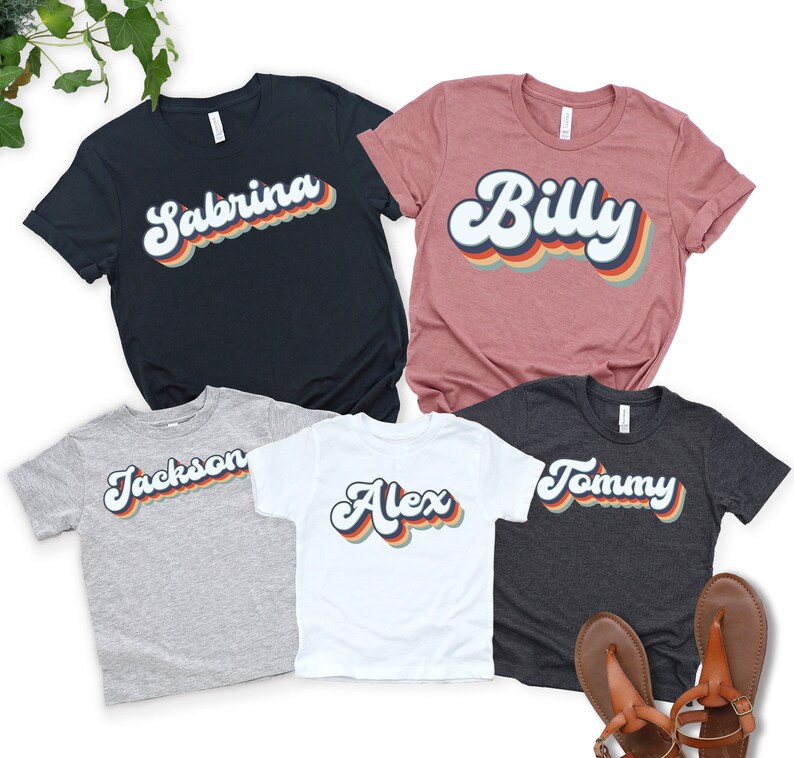 May include: Five t-shirts with retro-style font names printed on them. The names are Sabrina, Billy, Jackson, Alex, and Tommy. The shirts are in various colours, including black, pink, grey, white, and dark grey.