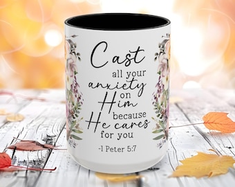 May include: White ceramic mug with a black interior, featuring floral designs and the text "Cast all your anxiety on Him because He cares for you -1 Peter 5:7". The mug has a wraparound floral pattern in shades of pink, purple, and green.