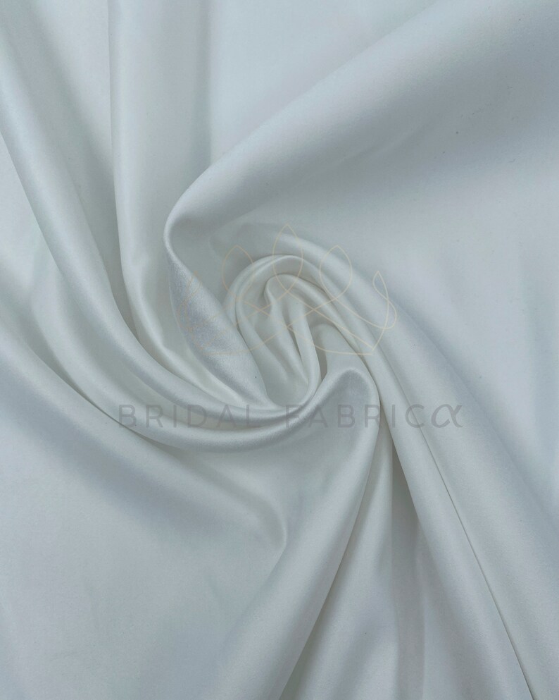 May include: White satin fabric, smooth and silky, with a soft drape. The fabric is folded and arranged in a way that shows its texture and flow.