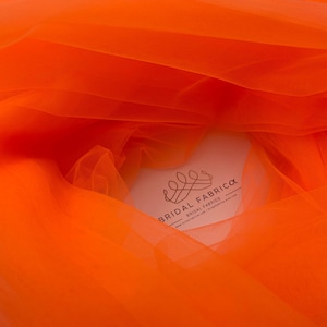 Könnte beinhalten: Orangener Tüllstoff, ein durchsichtiges und leichtes Material, mit dem Text "Bridal Fabrica" und "Bridal Fabrics" in Schwarz.