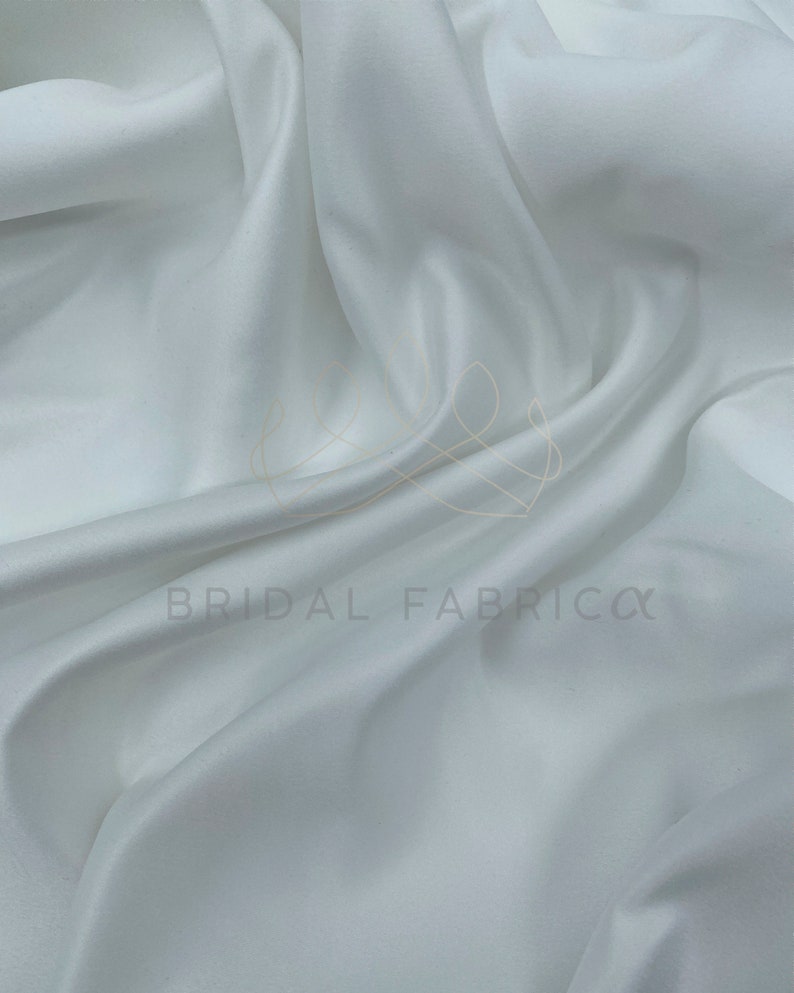 May include: White satin fabric, smooth and silky, with a subtle sheen. The fabric is draped and folded, showcasing its luxurious texture.