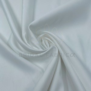 May include: White satin fabric, a smooth and luxurious material with a subtle sheen. It is perfect for creating elegant garments, home decor, and other projects.