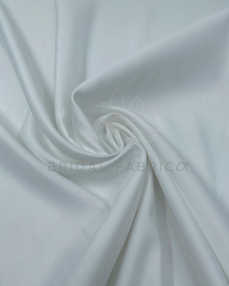 May include: White satin fabric, a smooth and luxurious material with a subtle sheen. It is perfect for creating elegant garments, home decor, and other projects.