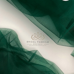 Puede incluir: Tela de tul verde oscuro, drapeada y en capas, sobre un fondo blanco. La tela es semitransparente, con textura y pliegues visibles. El texto "ST66" está en un óvalo blanco. También se ven el logotipo y el sitio web de Bridal Fabrica.