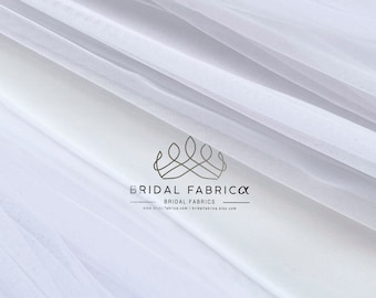 May include: White tulle fabric with a subtle sheen. The fabric is soft and delicate, perfect for creating a variety of projects. The fabric is labeled "ST03" and is sold by "Bridal Fabrica".