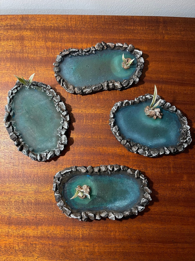 May include: Four small, oval-shaped, decorative ponds made of resin with a rocky edge. Each pond has a small green plant growing in the centre.