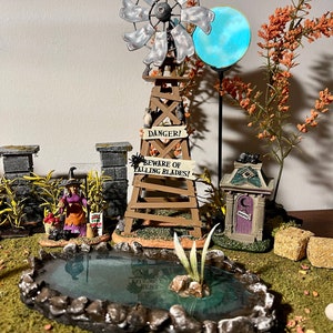 May include: A miniature Halloween scene featuring a witch, a pond, a windmill, a sign that reads "Danger! Beware of Falling Blades!" and a small house with a crescent moon on the door.