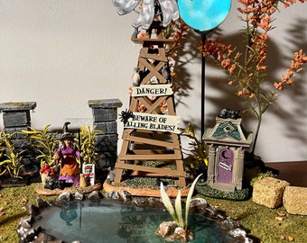 May include: A miniature Halloween scene with a witch, a pond, a windmill, a sign that reads "Danger! Beware of Falling Blades!" and a small house with a crescent moon on the door.