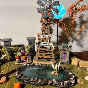 May include: A miniature Halloween village scene featuring a windmill, a pond, a small house, and a witch figure. The windmill has a sign that reads "Danger! Beware of Falling Blades!"