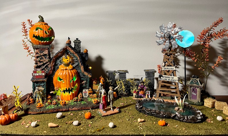 May include: A Halloween village scene featuring a spooky house, a windmill, a pond, and a sign that reads "Danger! Beware of Falling Pumpkins".