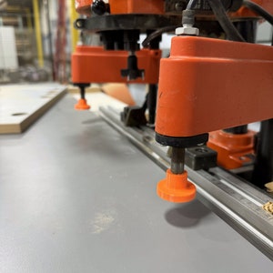 May include: Close-up of an orange industrial drilling machine with two drill bits. The machine is drilling into a grey surface.