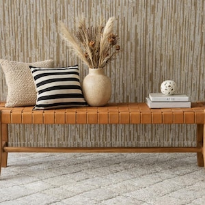 Puede incluir: Banco de madera con asiento de cuero tejido, con dos cojines, un jarrón con plantas secas y libros. El banco está colocado contra una pared texturizada. El banco mide aproximadamente 150 cm de largo.