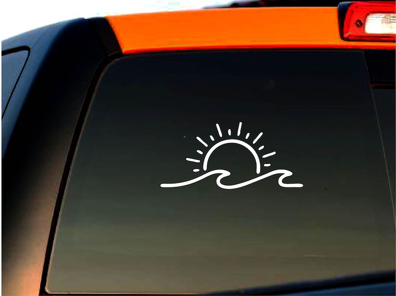May include: White vinyl decal of a sun setting over a wave. The decal is on a black car window.