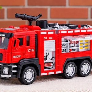 May include: A red toy fire truck with black accents, featuring a roof-mounted water cannon, side compartments with visible equipment, and white text including "Alloy truck," "FIRE RESCUE," "RESCUE," "CLF 5000," "119," and "WJ-008" on the body.