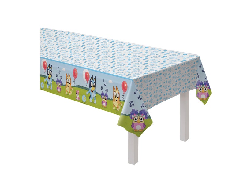 May include: Blue and green plastic tablecloth with a cartoon design featuring a dog and an owl. The tablecloth has a white background with a blue and white pattern.
