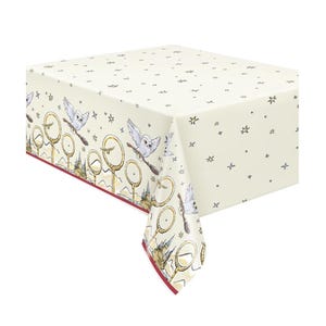 May include: Cream tablecloth with a repeating pattern of owls on brooms, golden hoops, and stars. The border has a maroon trim and a detailed illustration of a castle. A decorative table covering for themed events.