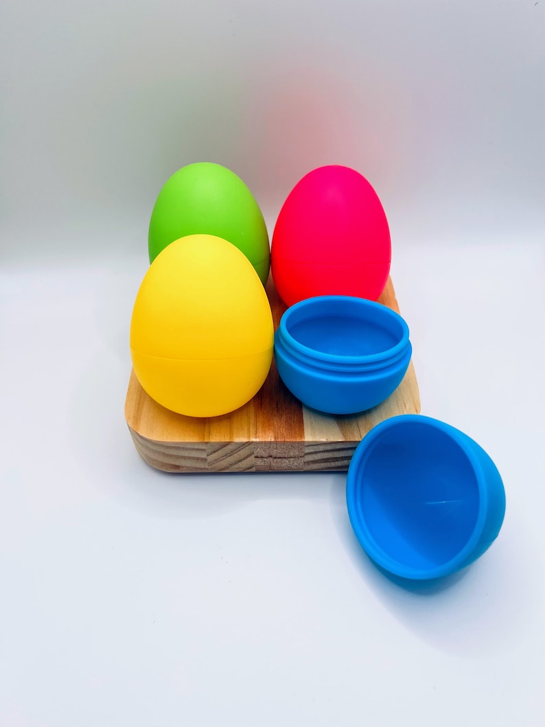 May include: Four colorful silicone Easter eggs on a wooden surface. Two of the eggs are closed, and two are open, revealing the inside of the eggs.