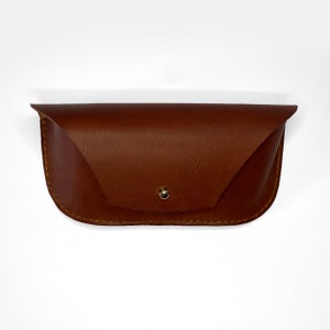 May include: A brown leather glasses case with a gold button closure.