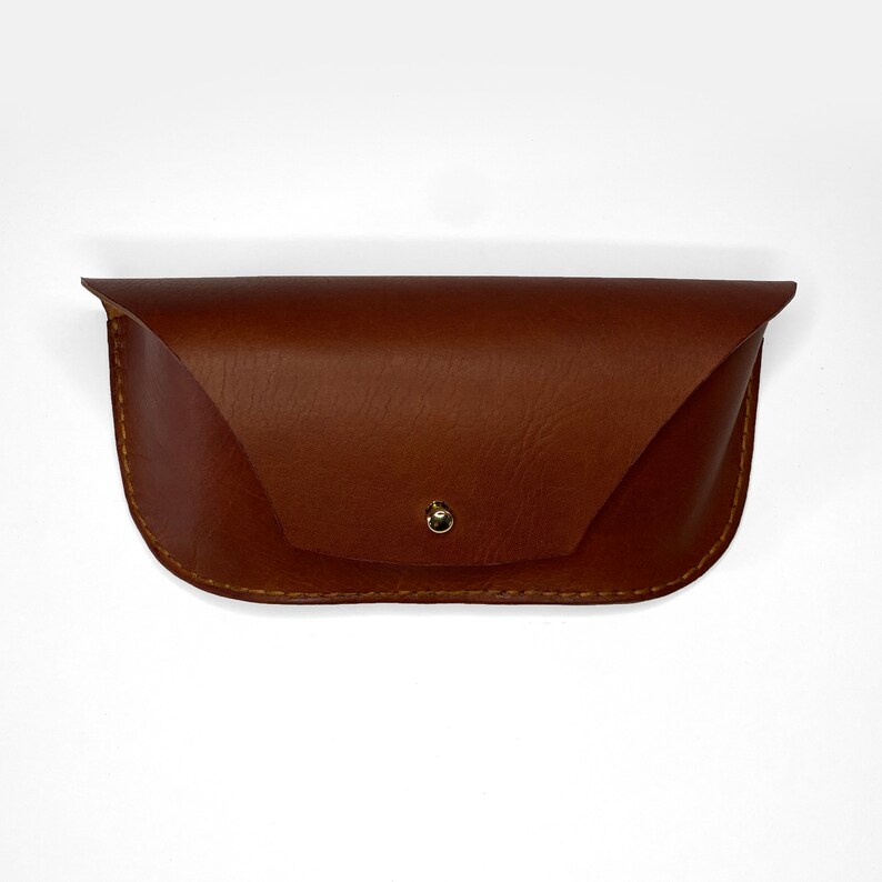 May include: A brown leather glasses case with a gold button closure.