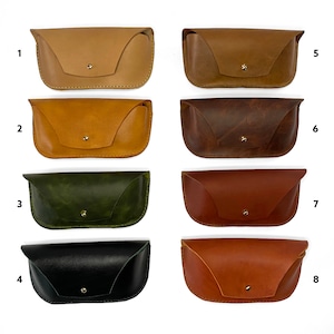 May include: Eight different colored leather eyeglass cases. The cases are all the same shape and size, with a flap that closes with a snap. The cases are arranged in two rows of four, with the numbers 1 through 8 printed below each case.