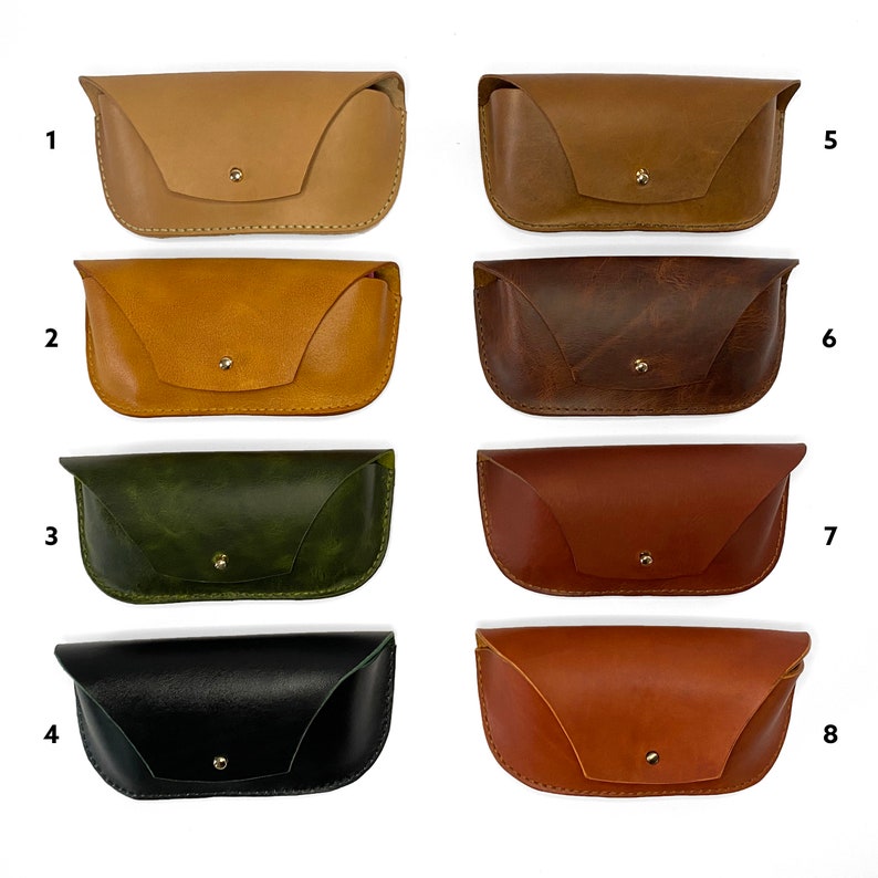 May include: Eight different colored leather eyeglass cases. The cases are all the same shape and size, with a flap that closes with a snap. The cases are arranged in two rows of four, with the numbers 1 through 8 printed below each case.