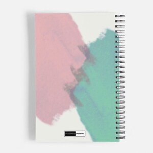 Op de afbeelding: Een spiraalgebonden notitieboek met een witte achtergrond en abstracte aquarelontwerpen in roze, blauw en groen. Het notitieboek heeft de tekst "DEYENVAMIC DESIGNS" onderaan gedrukt.
