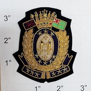 May include: A gold embroidered patch with a purple background. The patch features a crown, two flags, a wreath of leaves, and two fish. The patch is approximately 3 inches wide and 2 inches tall.
