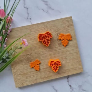 Peut inclure: Quatre emportes-pièces en forme de feuille en plastique orange sur une surface en bois. Les emportes-pièces sont de tailles et de formes différentes.
