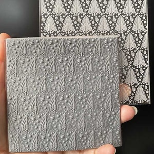 May include: Two clear acrylic stamps with a repeating pattern of white Christmas trees and snowflakes. The top stamp is a clear sheet with a white design. The bottom stamp is a grey sheet with a white design.