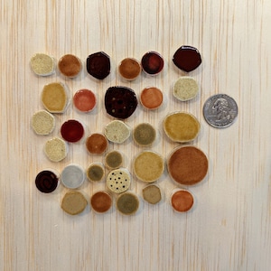 May include: Assortment of small, round and hexagonal ceramic tiles in various shades of brown, red, and beige. The tiles are arranged in a pattern on a light wood surface.