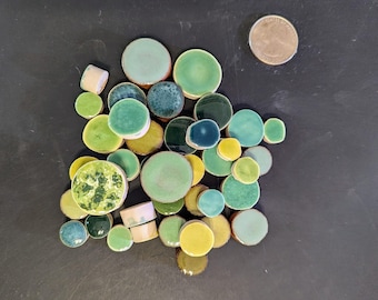 Pode incluir: Uma coleção de azulejos de cerâmica redondos em vários tons de verde, azul e amarelo. Os azulejos estão dispostos em um padrão aleatório e têm um diâmetro aproximado de 2,5 cm.