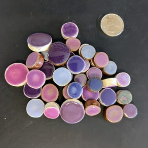 May include: A collection of round ceramic tiles in various shades of purple, pink, and blue. The tiles are arranged in a random pattern and have a glossy finish.