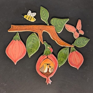 May include: A ceramic wall art piece featuring a branch with leaves, flowers, a bee, and a butterfly. The flowers are a coral color, and the leaves are green. The branch is brown, and the bee is yellow and white. The butterfly is pink.