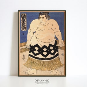 Könnte beinhalten: Ein japanischer Holzschnitt aus der Zeit, der einen Sumo-Ringer in einem schwarz-weißen, gemusterten Lendenschurz mit goldenen Fransen zeigt. Der Ringer steht in einem Ring vor blauem Hintergrund. Der Druck ist in einem dunkelgrünen Rahmen gerahmt.