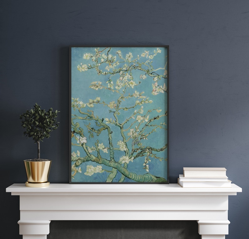 Puede incluir: Una impresi&oacute;n enmarcada de una pintura que representa un almendro en flor blanco sobre un fondo de cielo azul. La pintura est&aacute; en un marco negro y est&aacute; colgada en una repisa de chimenea blanca.
