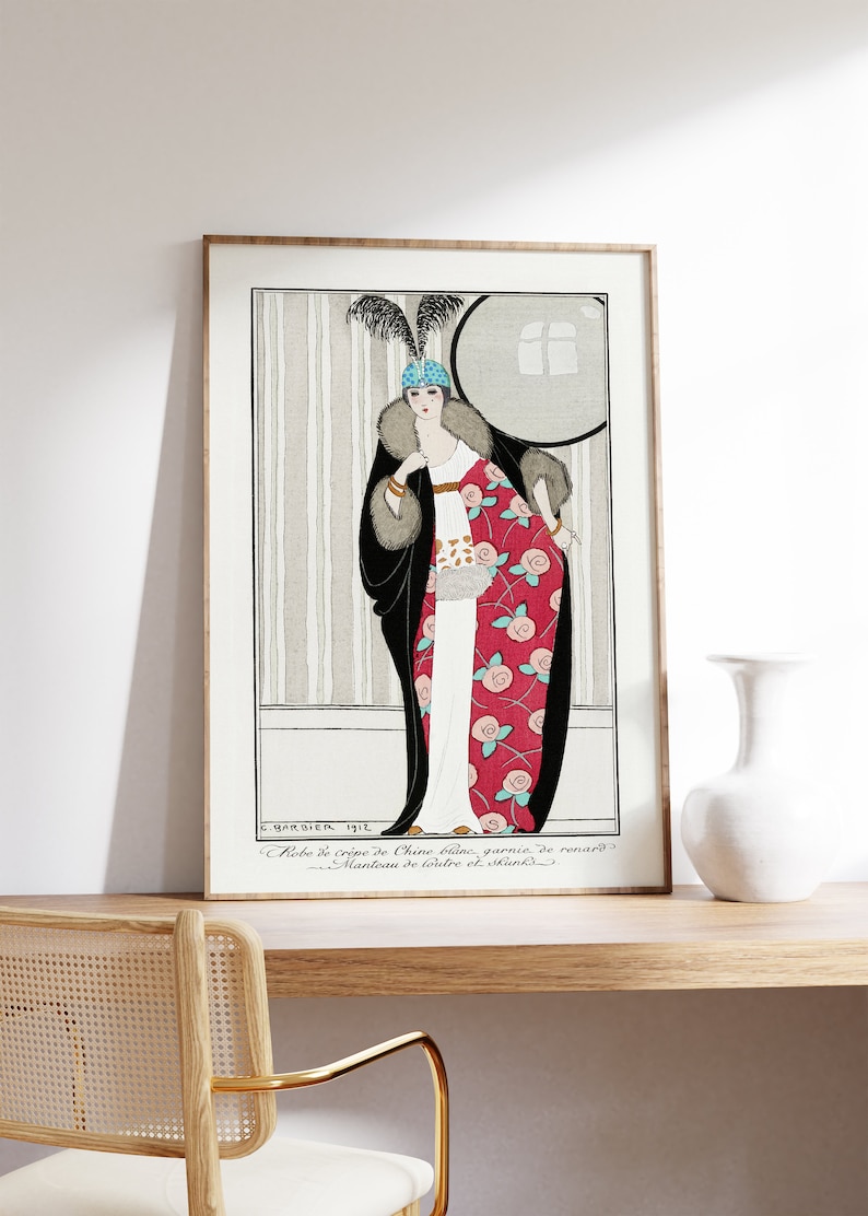 Op de afbeelding: Een vintage illustratie van een vrouw die een witte jurk draagt met een bloemenprint overlay en een zwarte bontjas. Ze draagt een blauwe hoed met veren en houdt een witte handtas vast. De illustratie is ingelijst en heeft de tekst "C. BARDIER 1912" en "Robe de crepe de Chine blanc, garnie de renard" en "Manteau de loutre et skunk" onderaan.