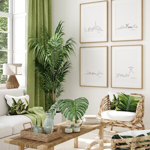 May include: A living room interior with a white couch, two wicker chairs with white cushions, a coffee table with a woven tray, and a green plant. The wall features four framed prints of city skylines.