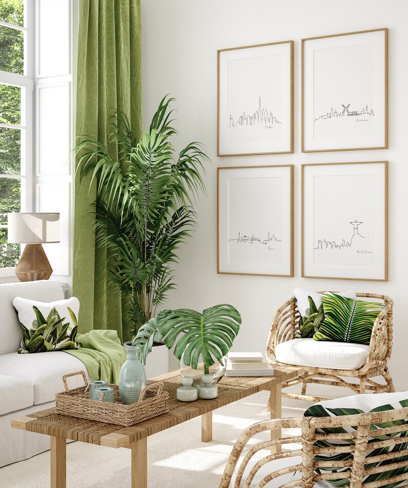 May include: A living room interior with a white couch, two wicker chairs with white cushions, a coffee table with a woven tray, and a green plant. The wall features four framed prints of city skylines.