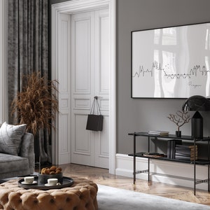May include: A stylish living room featuring a grey sofa, a buttoned ottoman, and a framed print of a city skyline. A black handbag hangs on the white door. A black marble lamp and console table add to the decor.