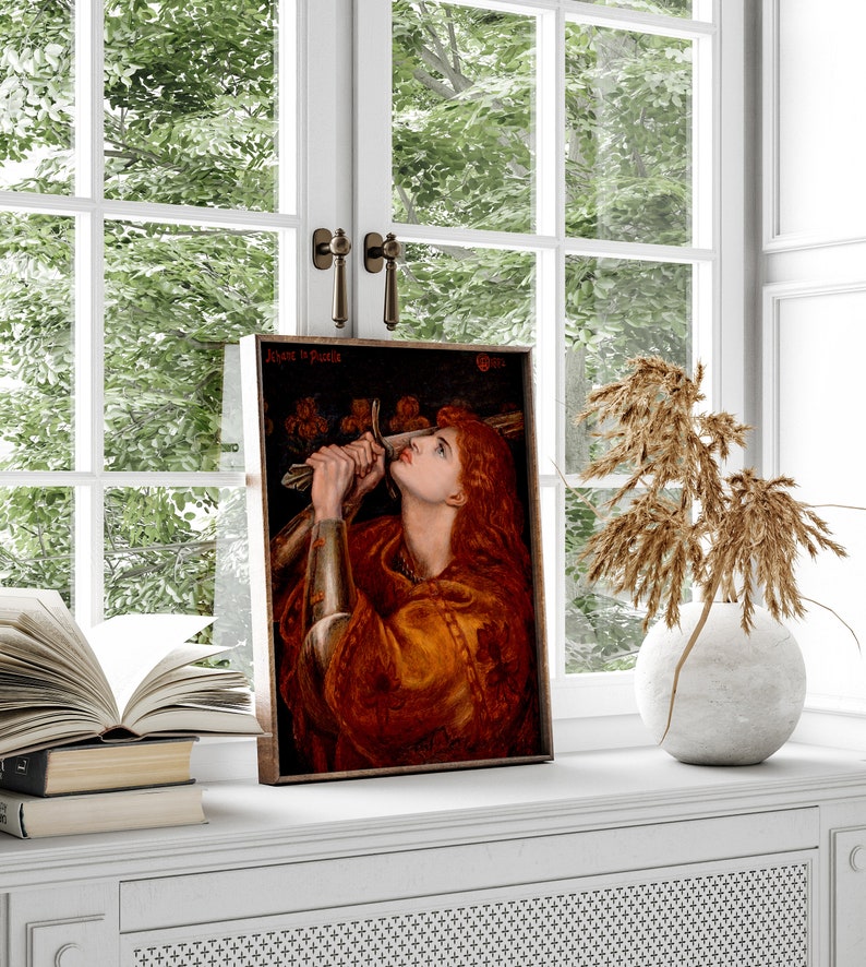 May include: A framed painting of a woman in a red and gold robe holding a sword. The painting is titled "Jehane la Paille" and is set against a dark background.