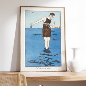 May include: A vintage illustration of a woman in a black swimsuit standing in the ocean. The illustration is in a frame and the text "Costume de bain" is at the bottom of the image.