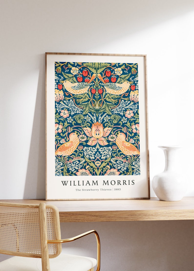 Op de afbeelding: Een ingelijste print van een vintage William Morris-ontwerp met een herhalend patroon van vogels, bloemen en bladeren op een donkerblauwe achtergrond. De tekst "WILLIAM MORRIS The Strawberry Thieves | 1883" is onder het ontwerp gedrukt.