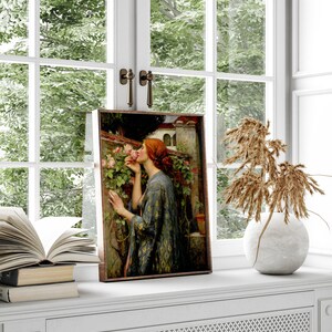 Op de afbeelding: Een ingelijst schilderij van een vrouw met rood haar die aan een roze roos ruikt in een tuin. De vrouw draagt een blauwe en gouden gepatroneerde robe. Het schilderij is geplaatst tegen een witte muur met een raam erachter.