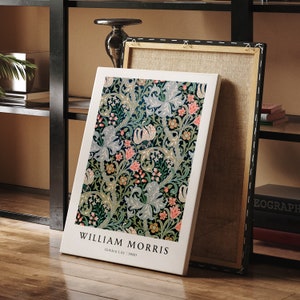 May include: A white canvas print featuring a floral pattern in shades of green, pink, and blue. The print depicts a stylised design of lilies and leaves. The text "William Morris" and "Golden Lily | 1880" is printed at the bottom of the canvas.