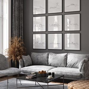 May include: A living room interior with a gray sofa, a coffee table, and a gray ottoman. The wall is painted gray and features nine framed black and white line drawings of city skylines. The drawings are arranged in a grid pattern.