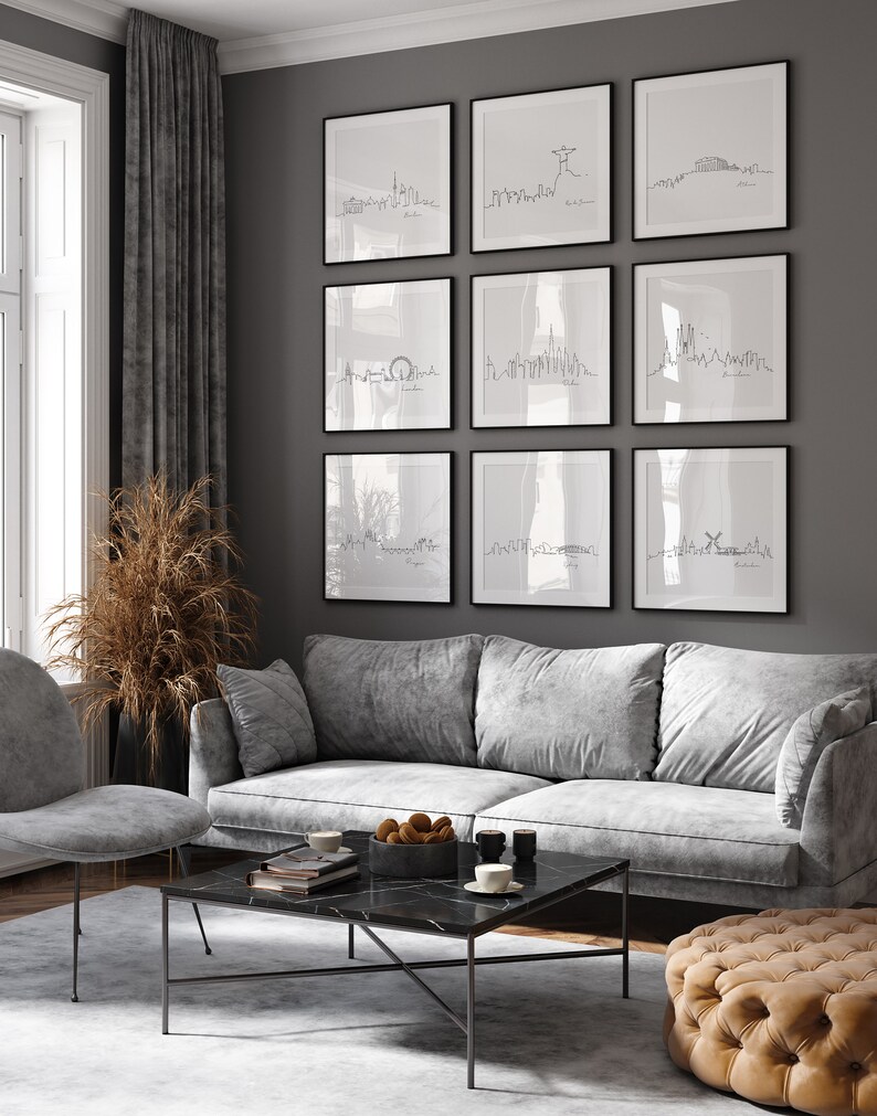 May include: A living room interior with a gray sofa, a coffee table, and a gray ottoman. The wall is painted gray and features nine framed black and white line drawings of city skylines. The drawings are arranged in a grid pattern.